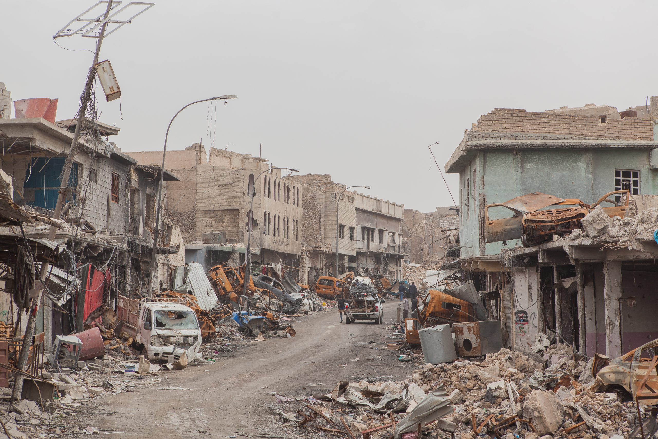 A street lined with damaged buildings, destroyed cars, and rubble.