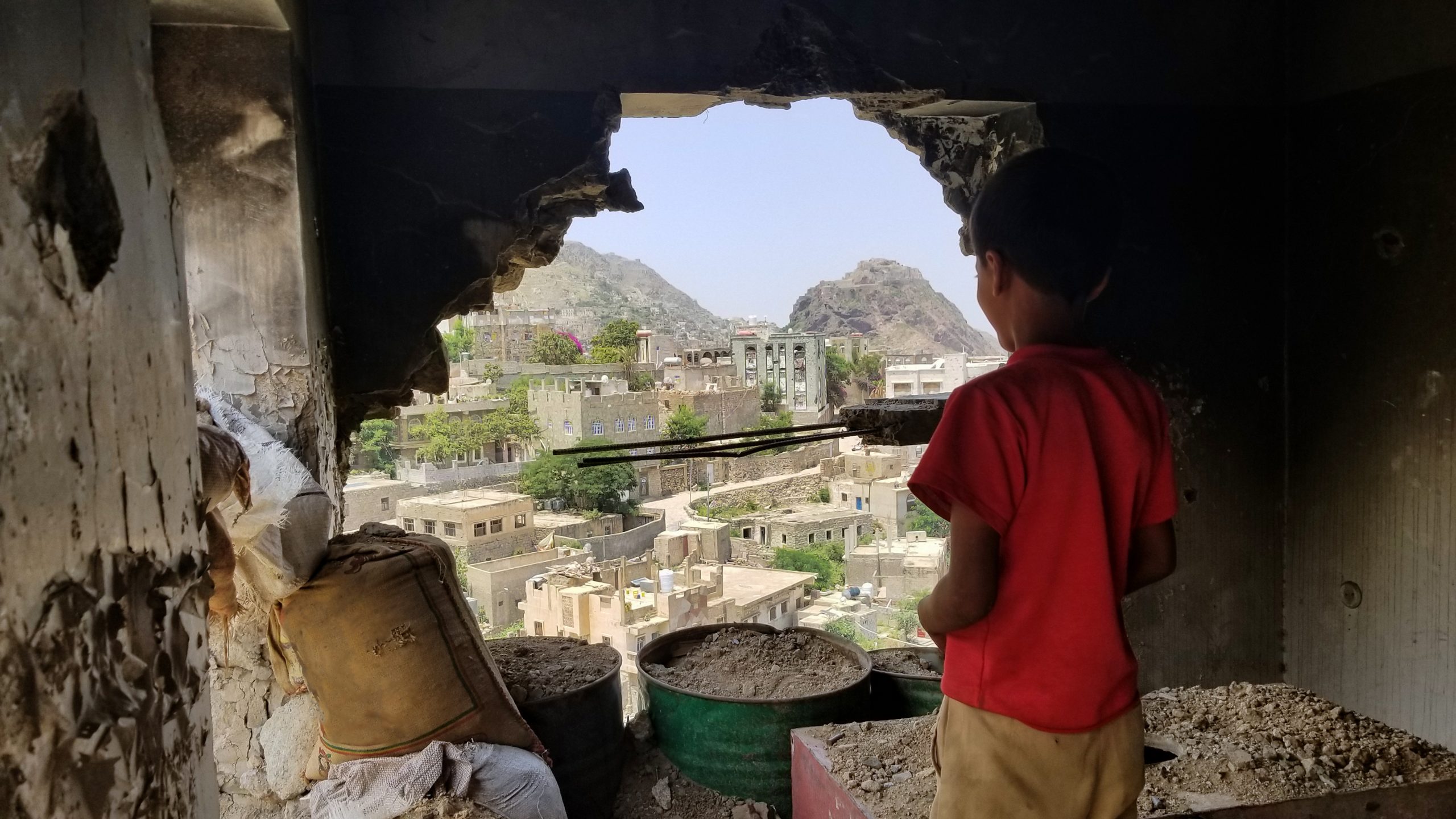 A young boy looks out through the hole in a damaged building