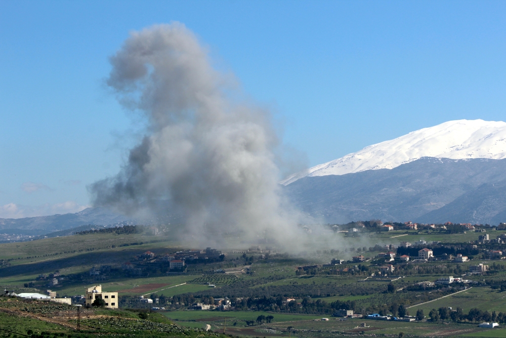 Smoke rises above a town in front of the mountains