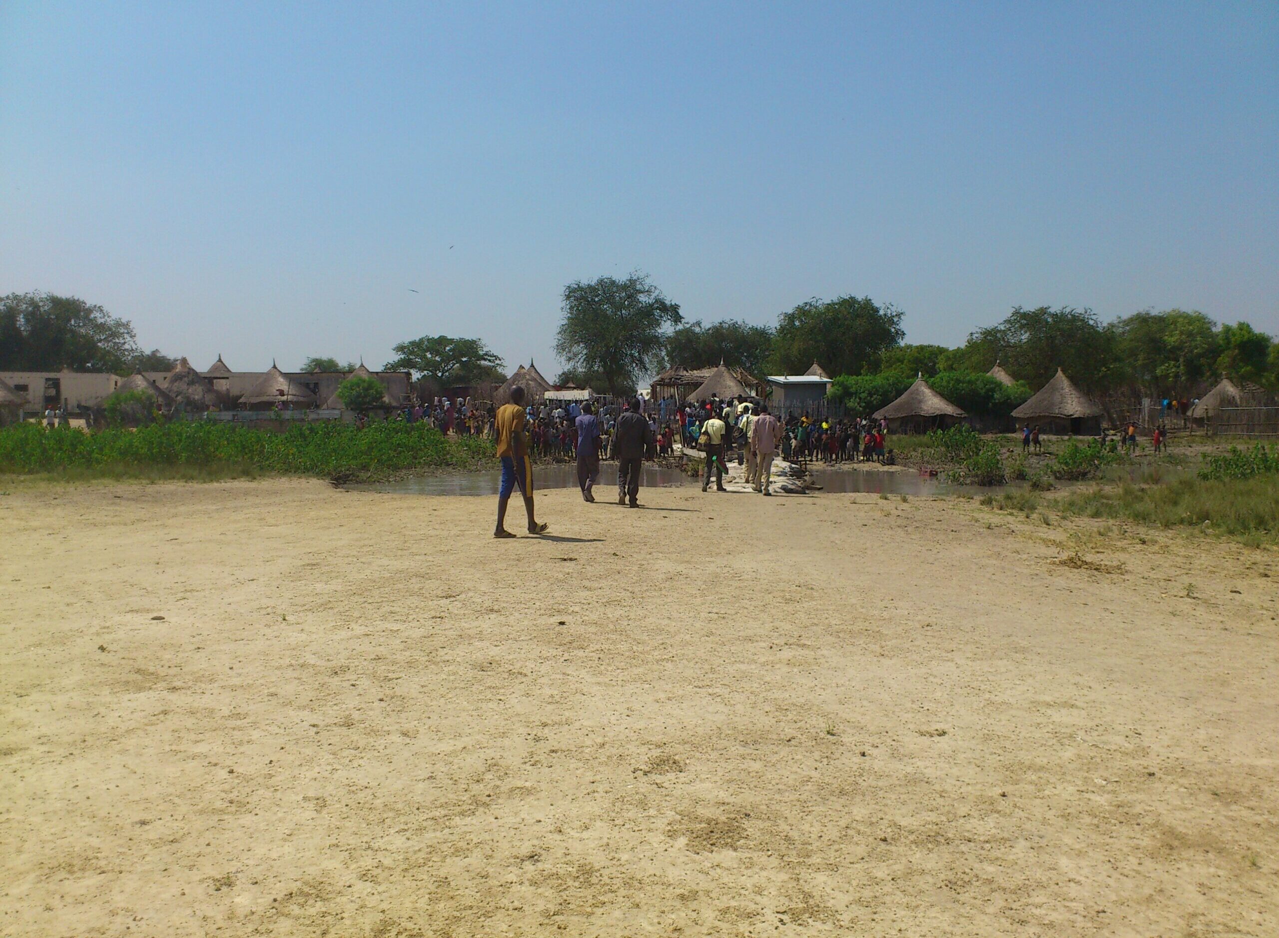 A crowd gathers in front of a row of huts