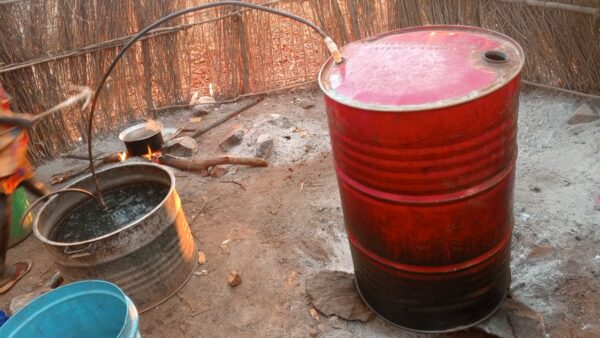 Red barrel with lid and pipe going into a wide bucket containing liquid, with another pipe going out